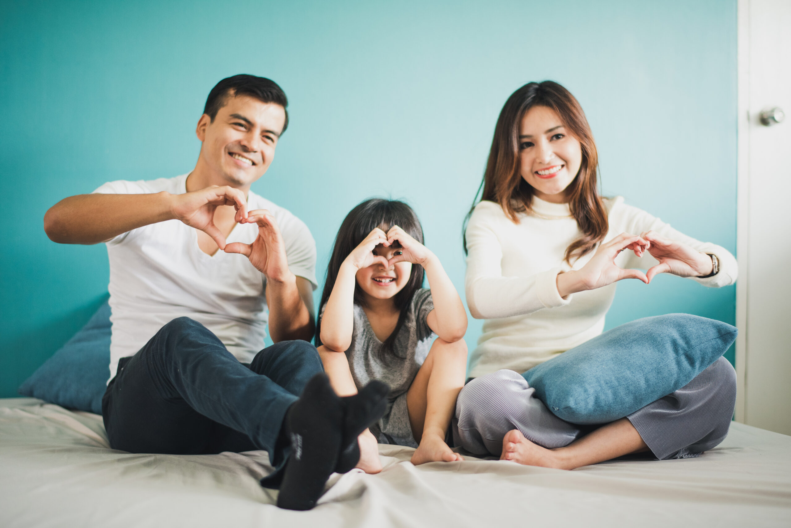Happy Cheerful smiling enjoy, Young Family mother father and daughter sitting on the bed, blue background